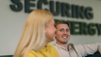 Två personer sitter i en soffa med texten "SECURING ENERGY" synlig i bakgrunden. Deras ansikten är suddiga.