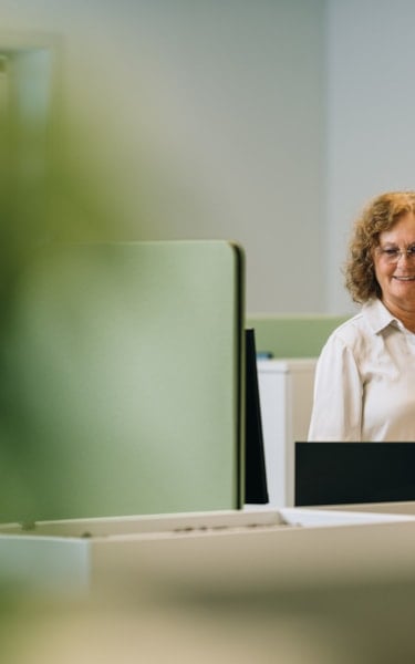 Two women stand in an office near a desk with a laptop.