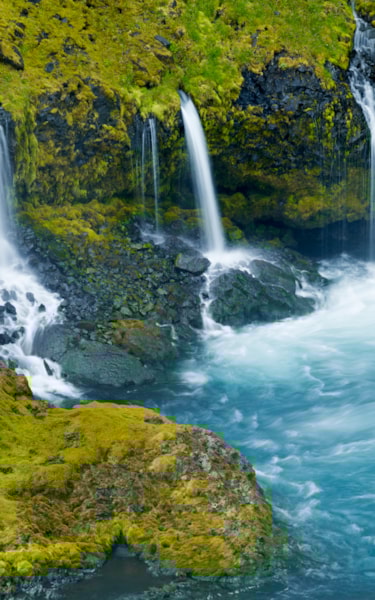 Small waterfalls cascade down a mossy cliff into a clear blue pool.