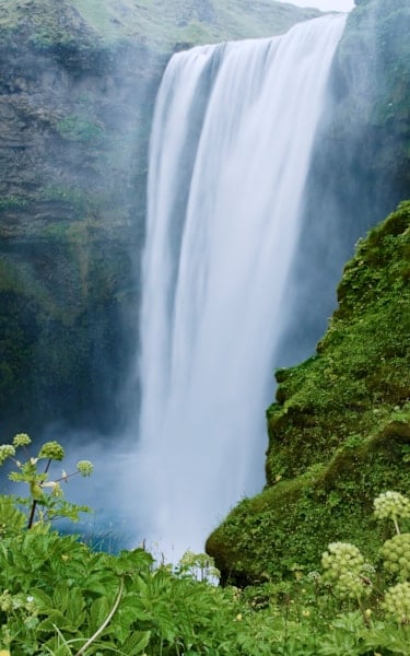 Stort vattenfall omgivet av frodig grönska, som rinner ner i en dimmig bassäng.